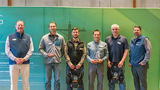 Image of a several employees standing in front of a graphic showing power lines.