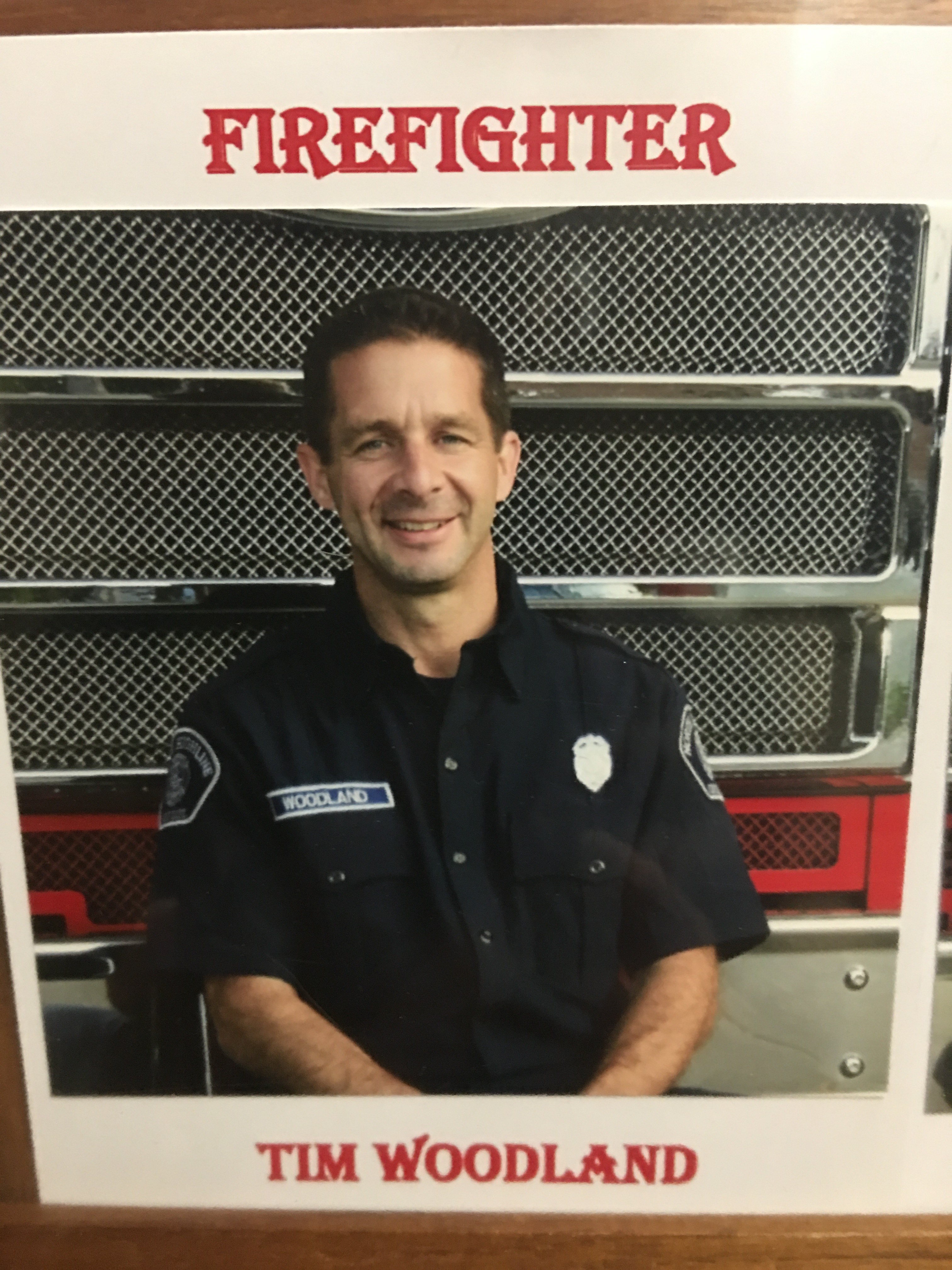 Image of Tim in his firefighter's uniform, which is blue and has a badge over his left chest. On the right side of Tim's chest is his nametag.