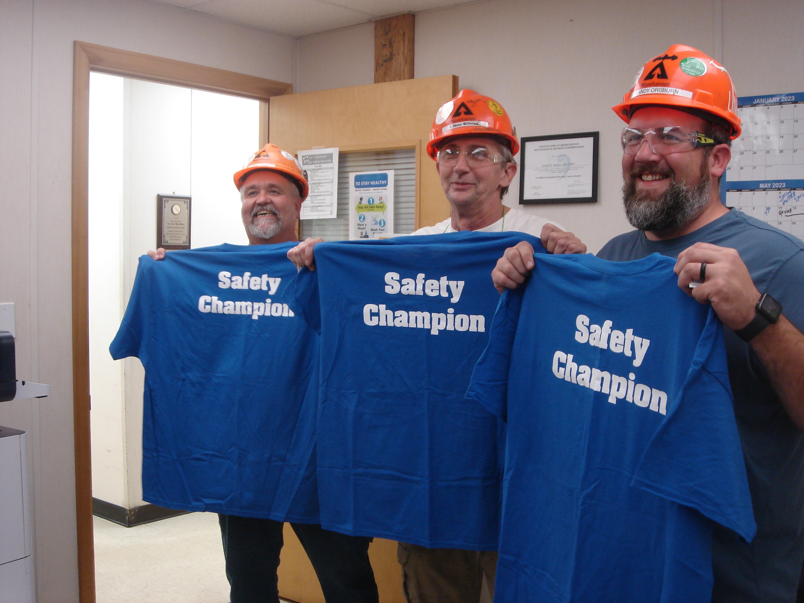 Image of three Buckhannon workers receiving "Safety Champion" t-shirts for helping a coworker iwth an overhead door issue. The shirts are blue with white lettering.