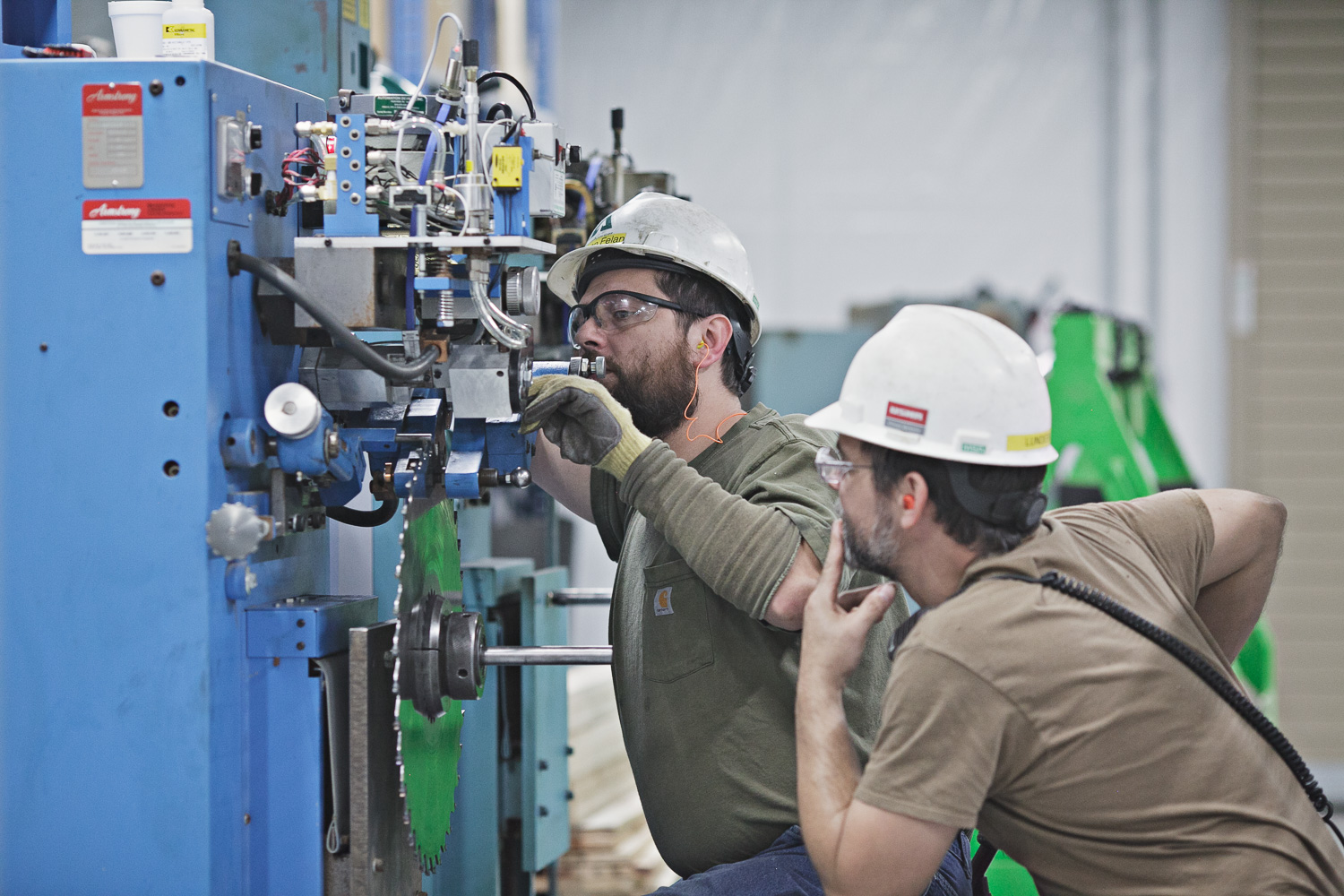 Two individuals wearing hardhats are performing maintenance on machinery.