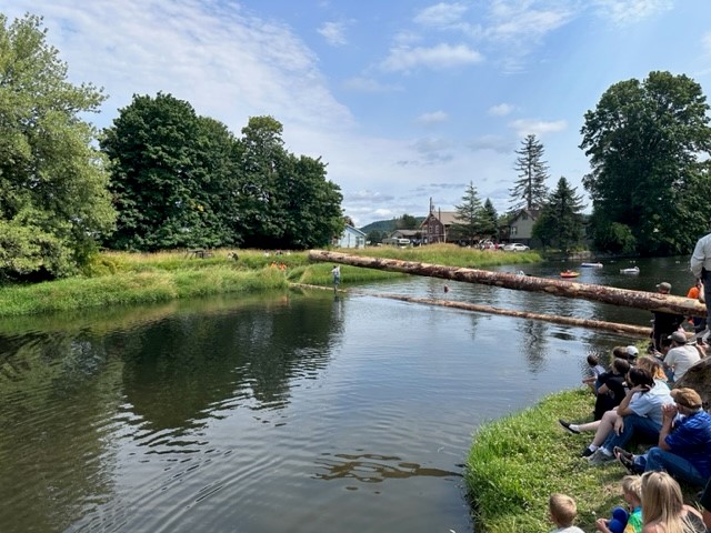 Image of spectators lining the banks of the Rock Creek River to watch the boom stick run.