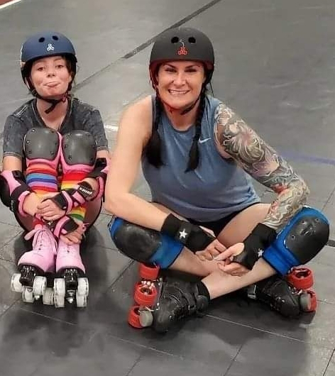 Image of Amber teaching her niece how to rollerskate. Both have protective gear on, including wrist protectors, knee pads and helmets.