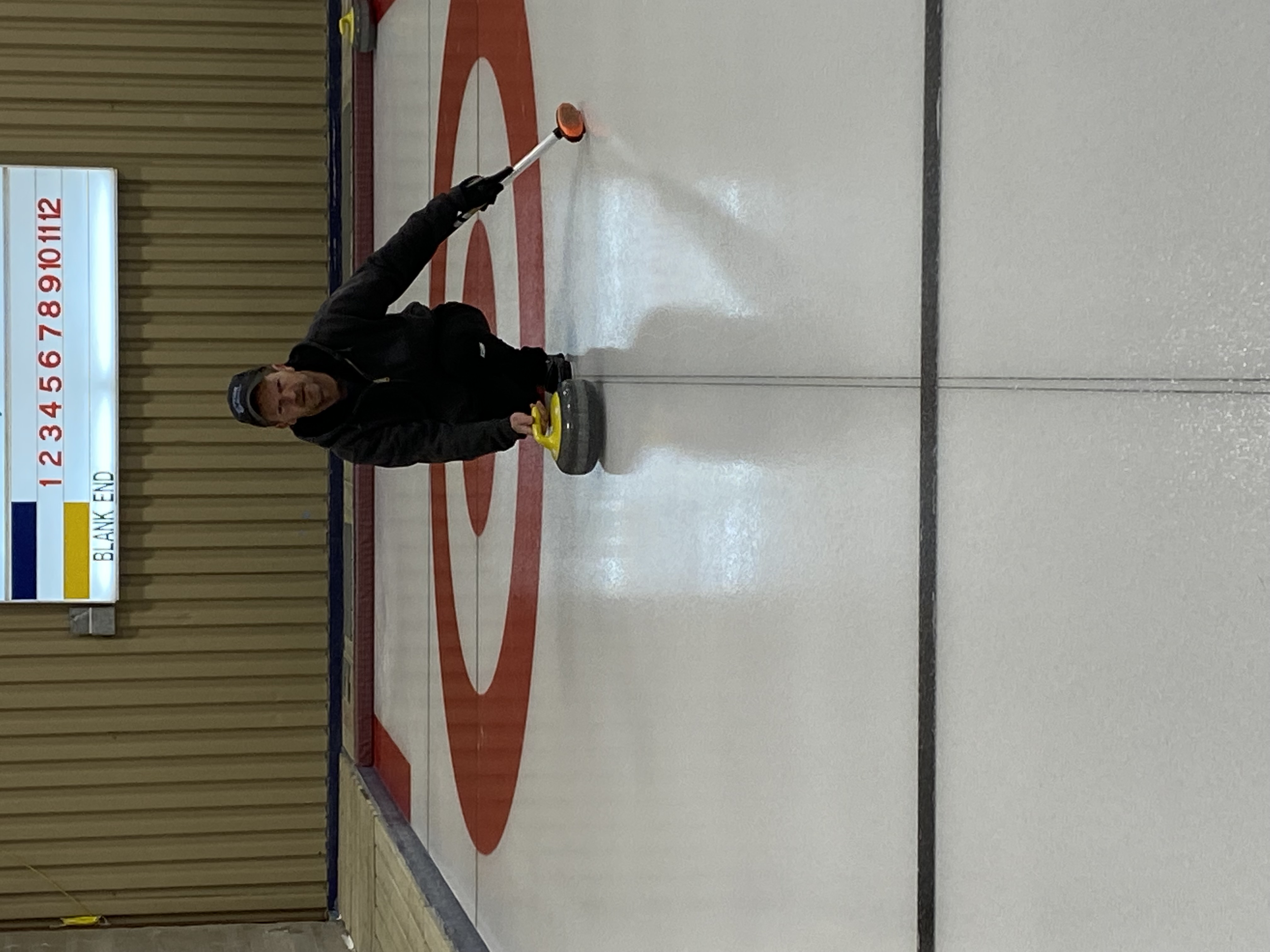 Image of Gary sliding a stone on one of the ice sheets he helps maintain.