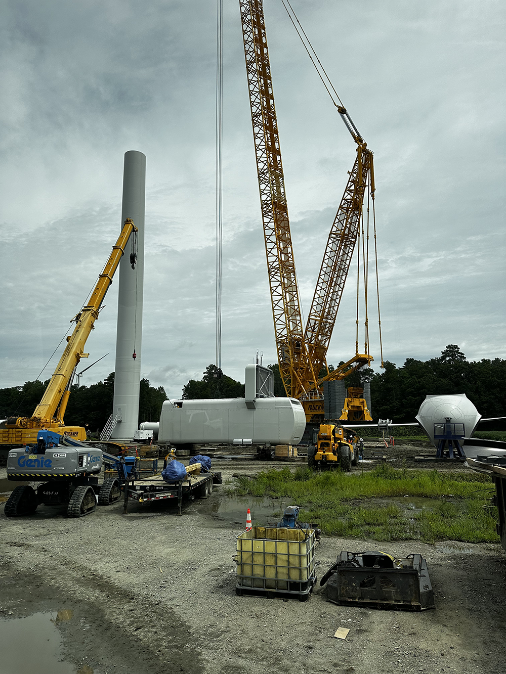 Image of cranes hoisting piecs of a wind turbine into place.