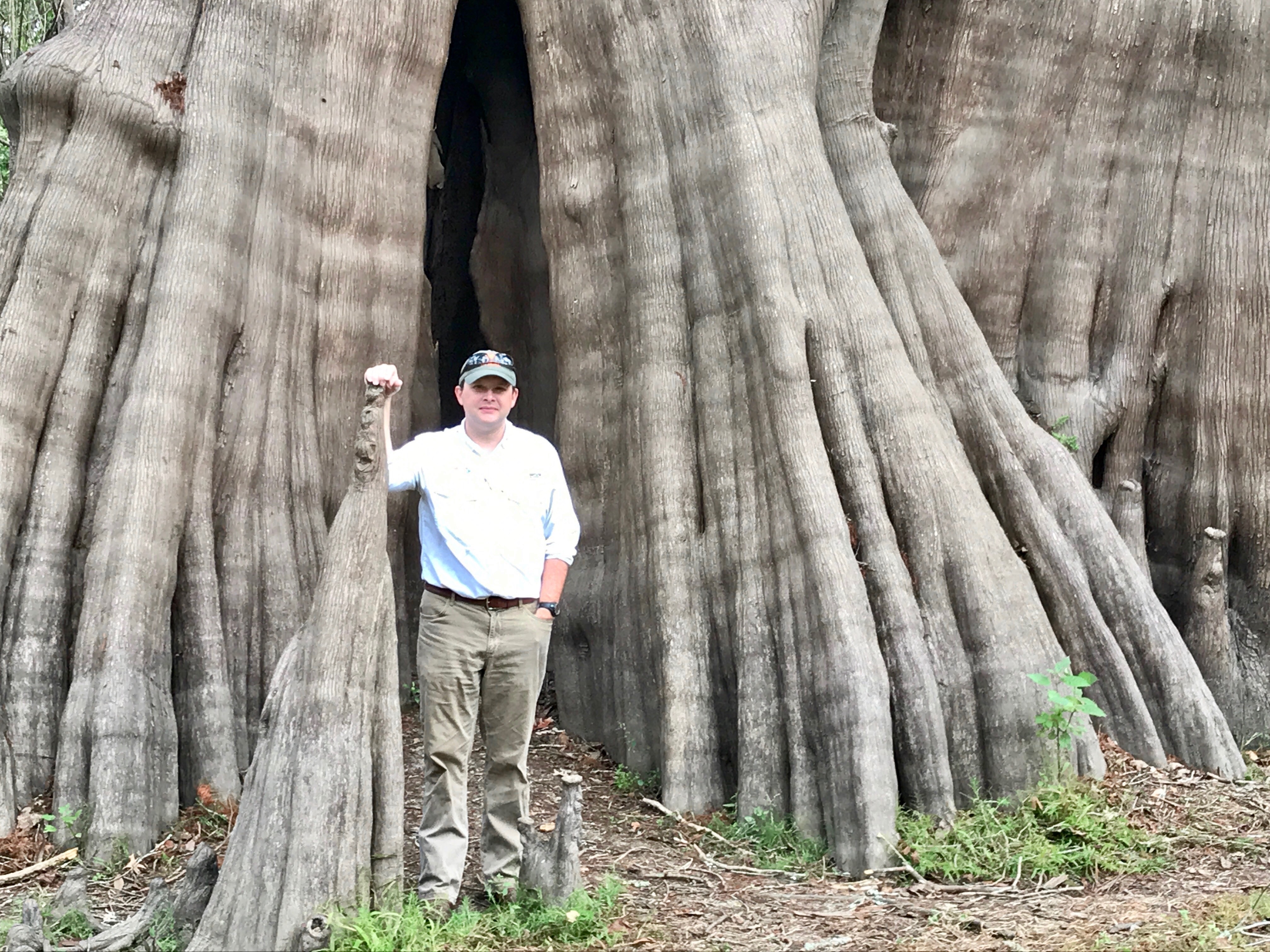 Image of Alex standing in front of a massive cypress tree on a national wildlife refuge.