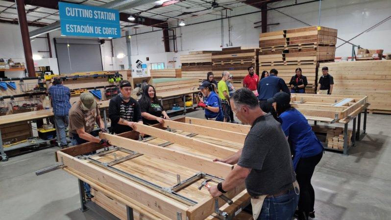 Image of volunteers at work in the CHUCK Center. A group of five people are lining up beams and attaching them to a piece of plywood.