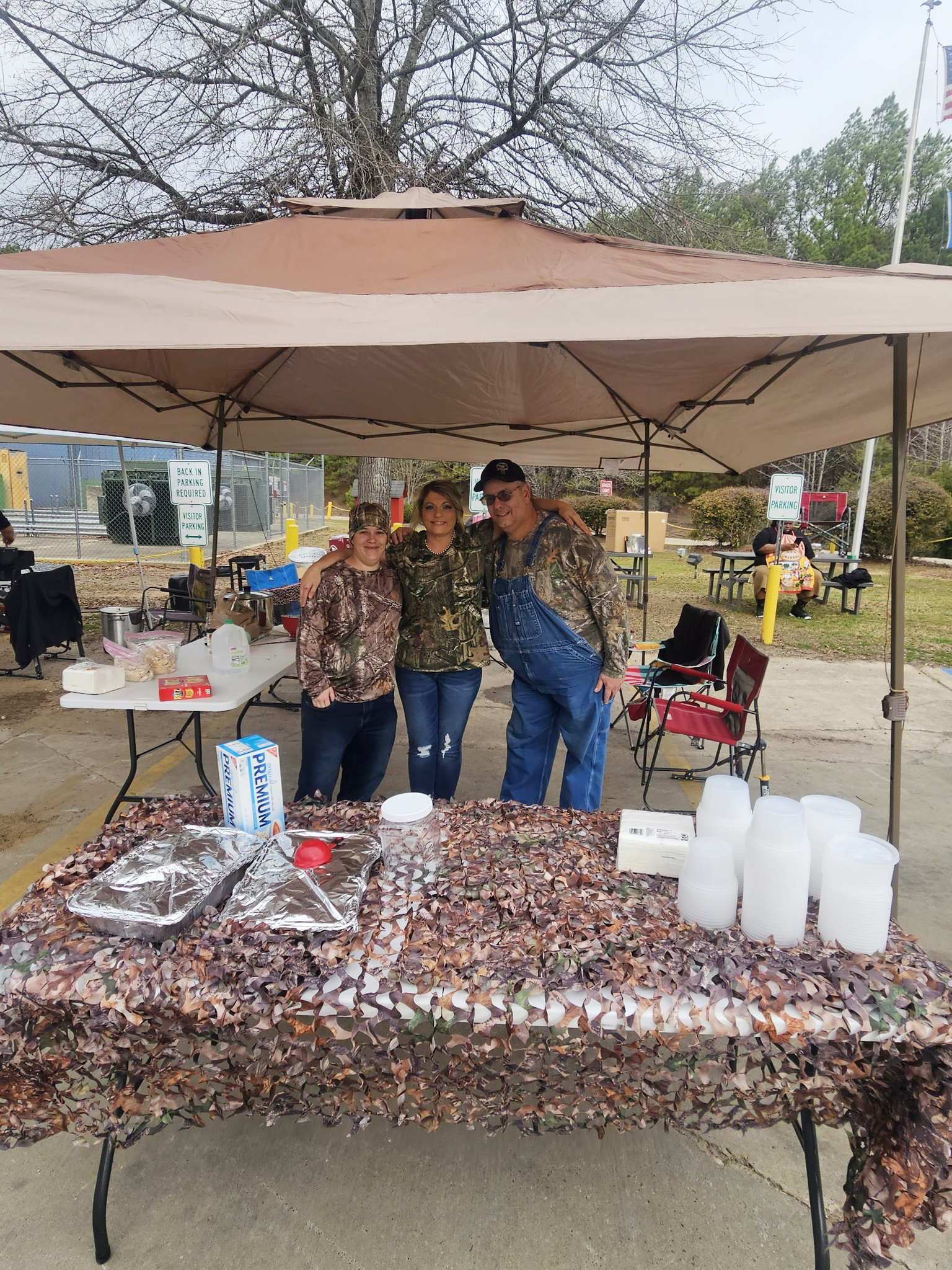 Image of Brandi Smith, Shonna Sullivan and Sam McCain. All three are dressed in camouflage shirts to match their 'Hunting for a Cure' theme. The table in front of them is also covered in camouflage material with food containers on top.