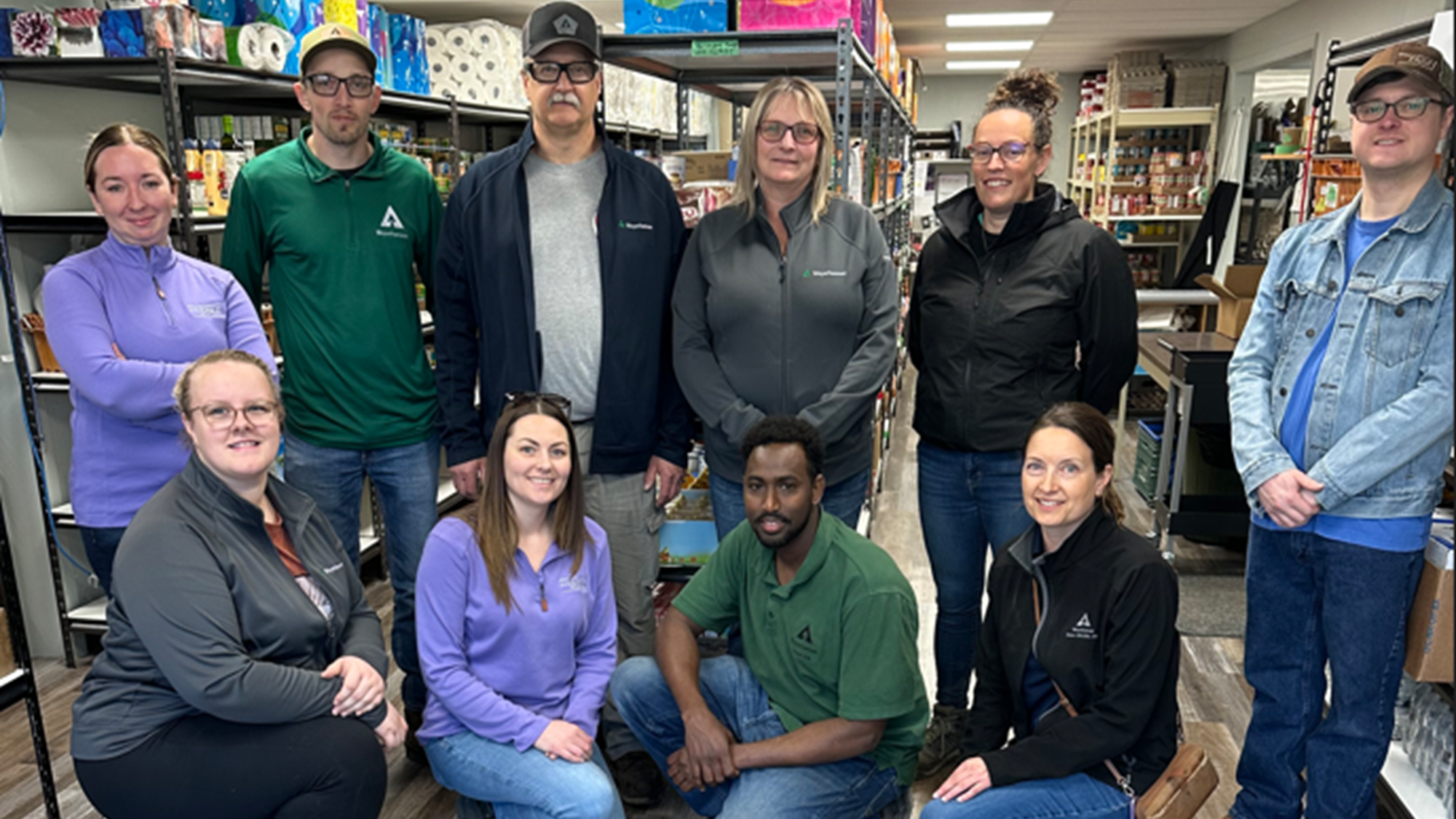 Image of Abdul and the Edson OSB team volunteering at the food bank. Abdul is crouching in the first row with nine colleagues surrounding him.