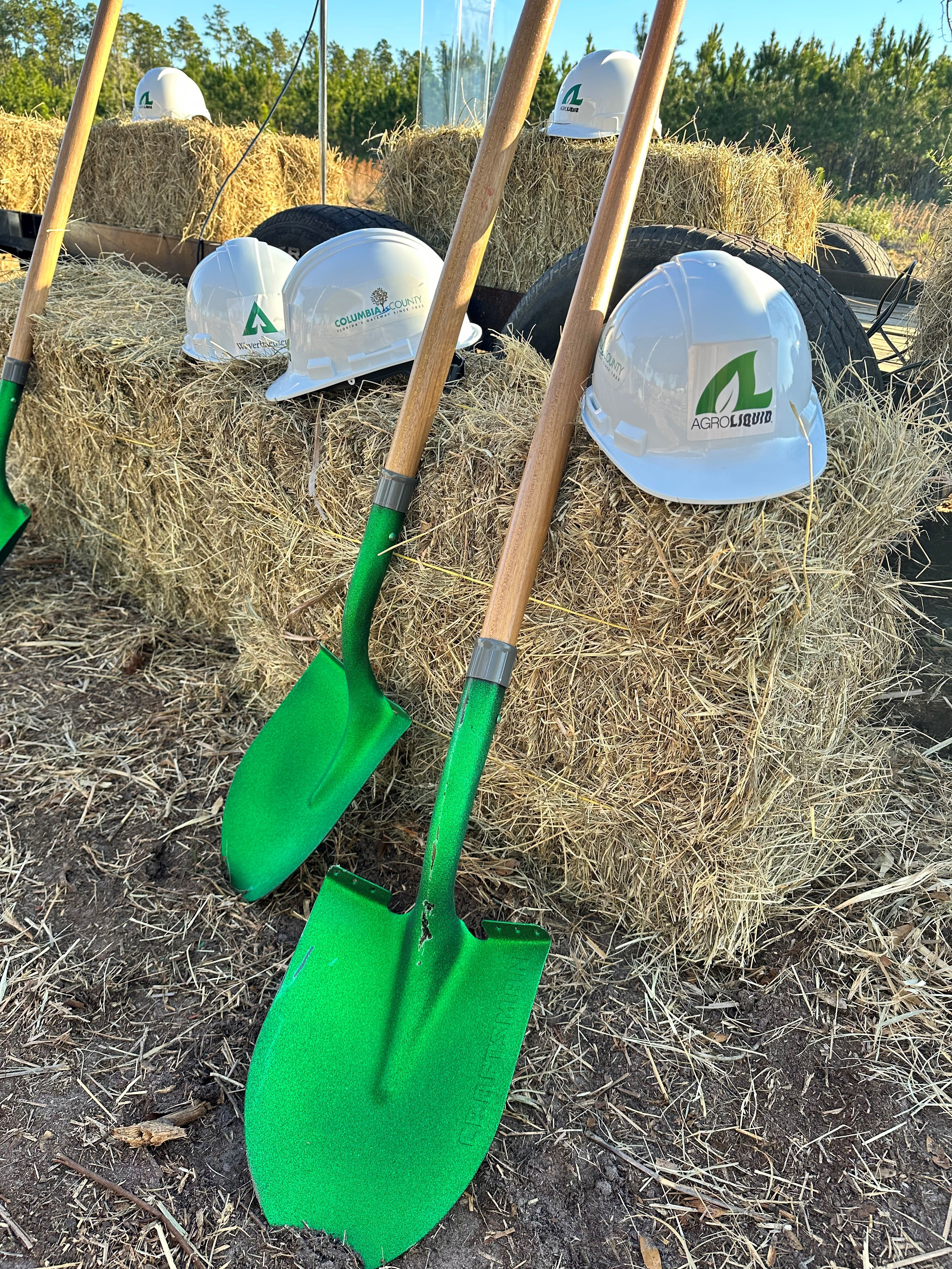 Image of green-spaded shovels and hard hats featuring the Weyerhaueser, AgroLiquid and Columbia County logos used during the groundbreaking ceremony for the North Florida Mega Industrial Park.